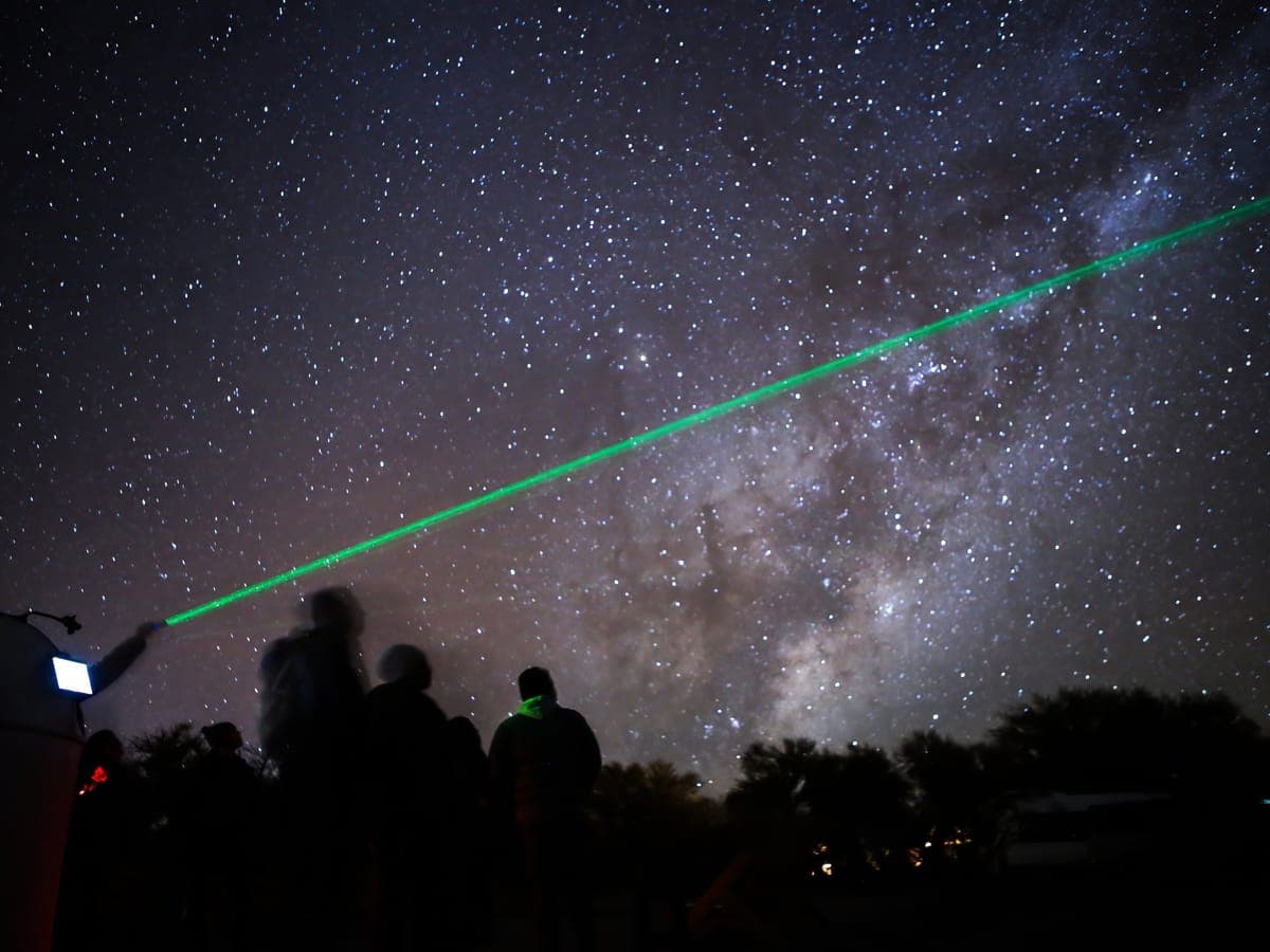 The guide points a green laser at the Milky Way while the group watches the sky over San Pedro de Atacama