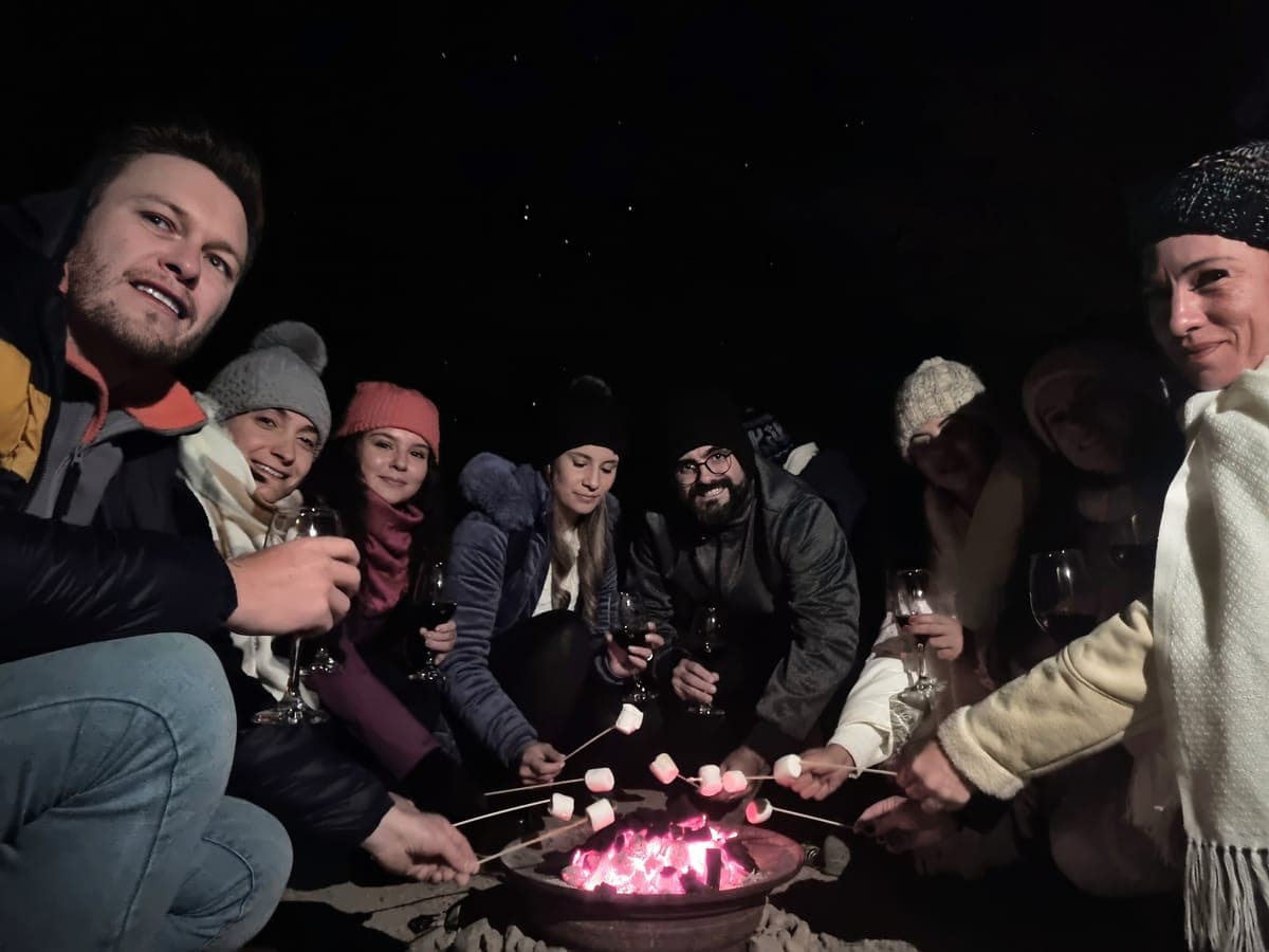 Travellers with glasses of wine toast marshmallows by the fire pit after the stargazing session